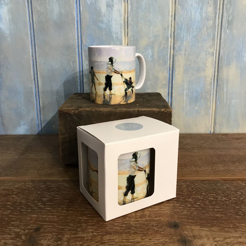 Ceramic mug illustrated with the painting Across the Beach of a family walking behind their mother who is pushing a pram across the sand and the sea in the distance. The convoy is followed by the pet dog. One mug is shown in a gift box.