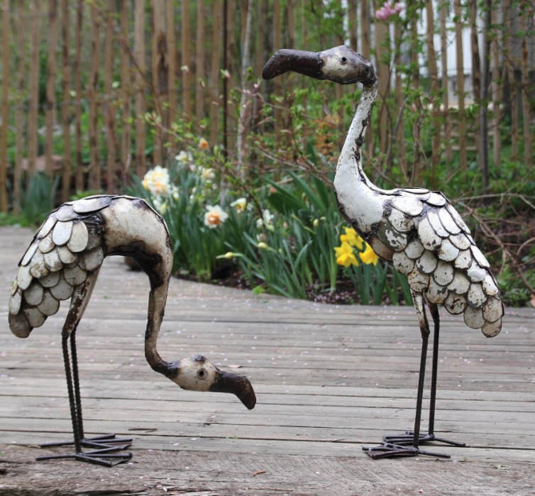 metal flamingo sculptures one stooping one standing. In burnished metal with cream highlights.